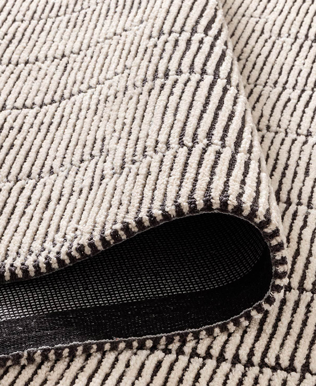 The cream and black patterned rug is folded back on itself, showing the tufted detail and texture. The cream and black patterned rug is folded back on itself, showing the tufted detail and texture.