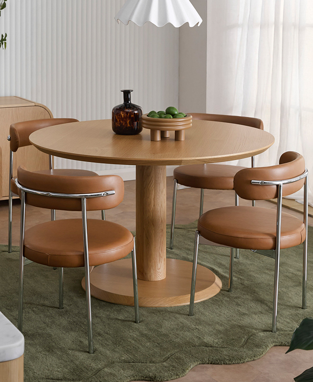 The round pedestal table is on a rectangular green rug, and rounded tan and chrome chairs are positioned around it.