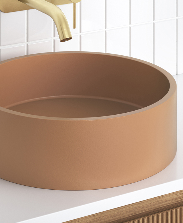Round terracotta countertop basin with brushed brass wall spout, white square tile splashback on white vanity.