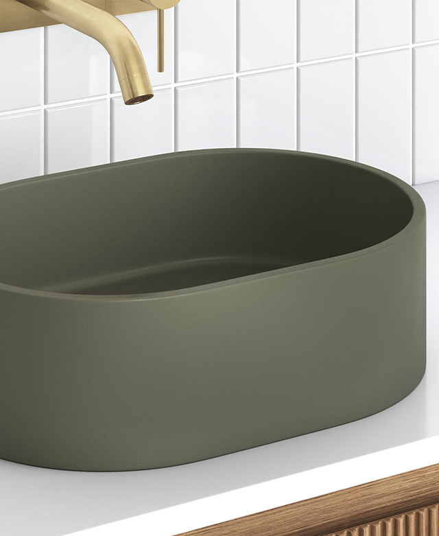 Matte olive green oval countertop basin beneath brushed brass wall spout; white tiled splashback.