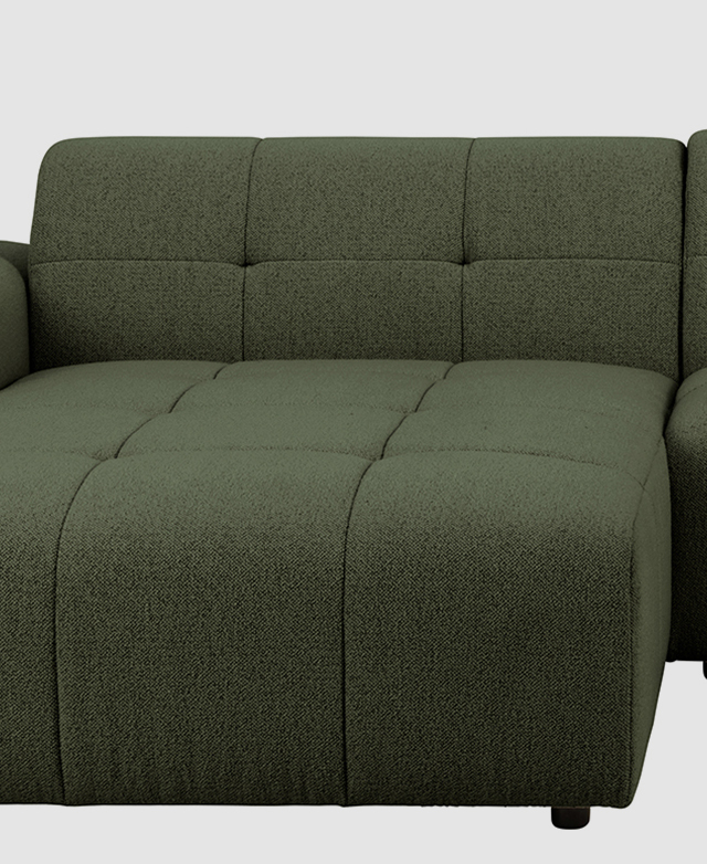 The chaise end of the green sofa is shown front on, highlighting the geometric biscuit tufting.