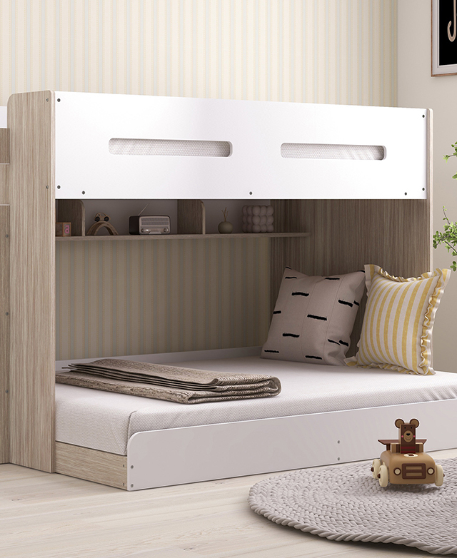 A white assembled single-over-double bunk bed is dressed with simple bedding and cushions, with a round rug next to it.