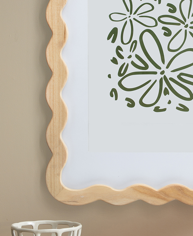 The poplar MDF wavy frame holds a green floral image within a white mat. It's hung on a taupe wall.