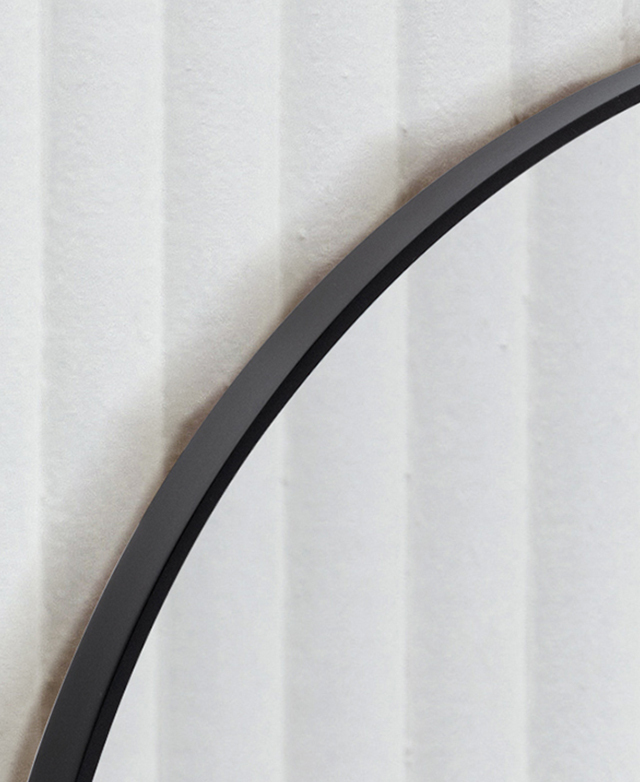 Magnified image of the mirror underscores the smooth, narrow black frame against a fluted wall.