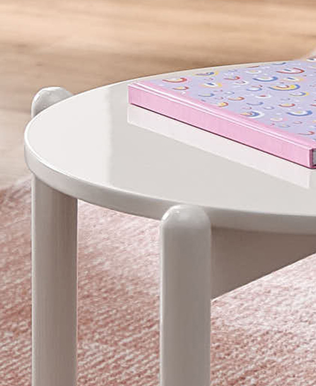 A rainbow book is on top of the round, glossy white children's table.