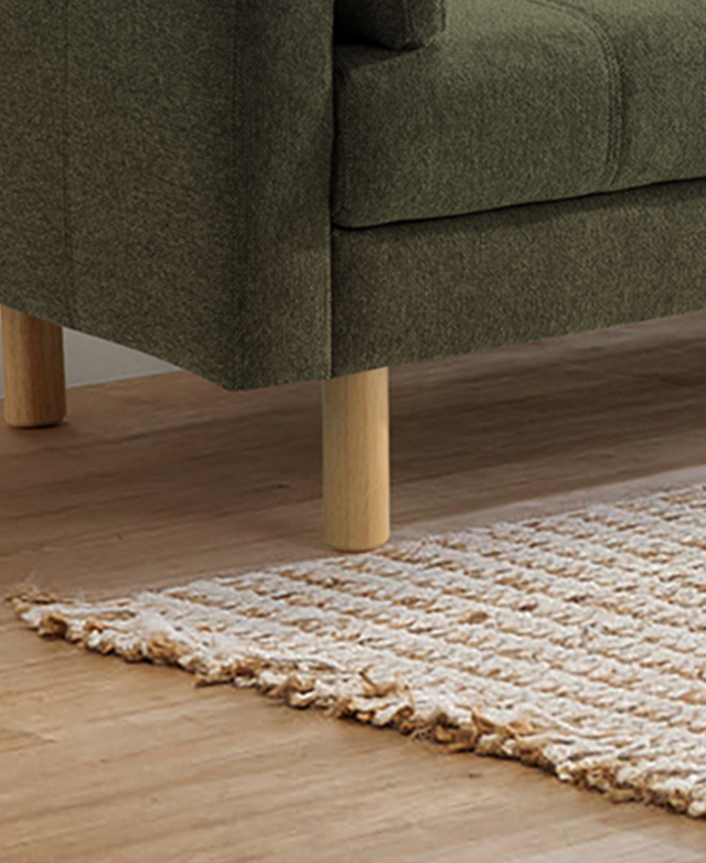 Cylindrical rubberwood legs of the green sofa are pictured next to a jute rug.