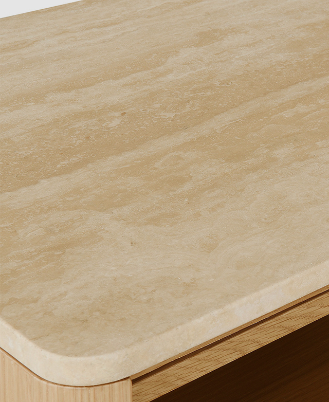 The earthy-toned travertine top surface of the bedside table is smoothly finished and features rounded corners.