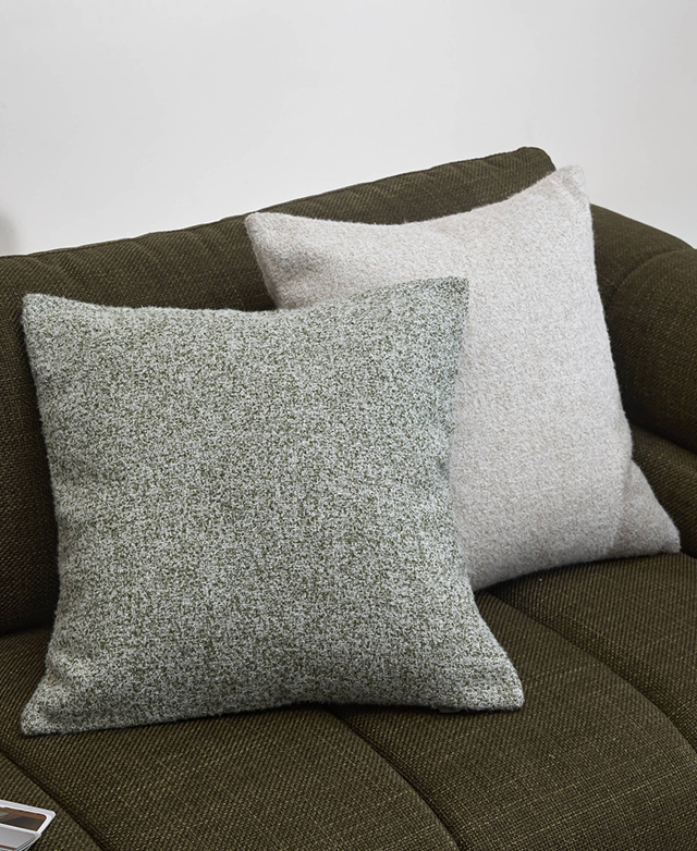Two cushions - one green, one cream - are well-filled and positioned on a green sofa.