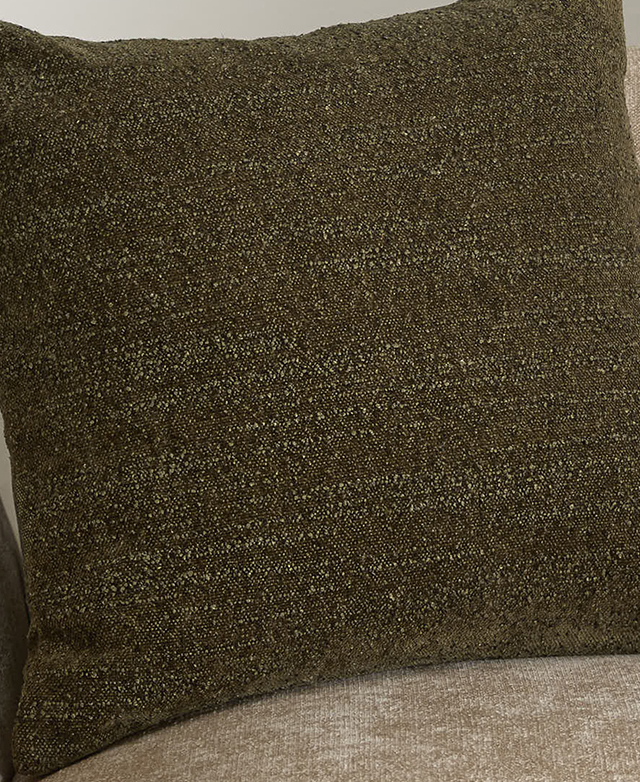Rich green boucle fabric of a square cushion is pictured up close.