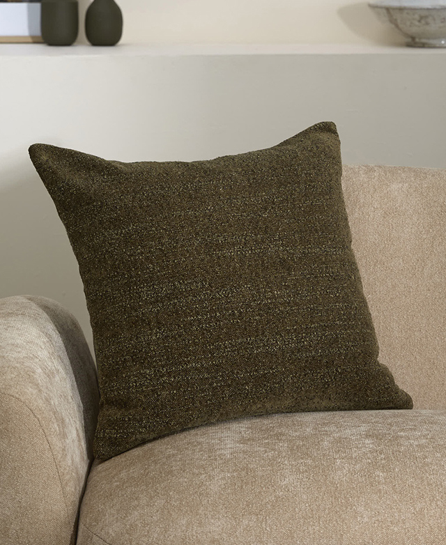 The square green boucle cushion is on a taupe sofa.