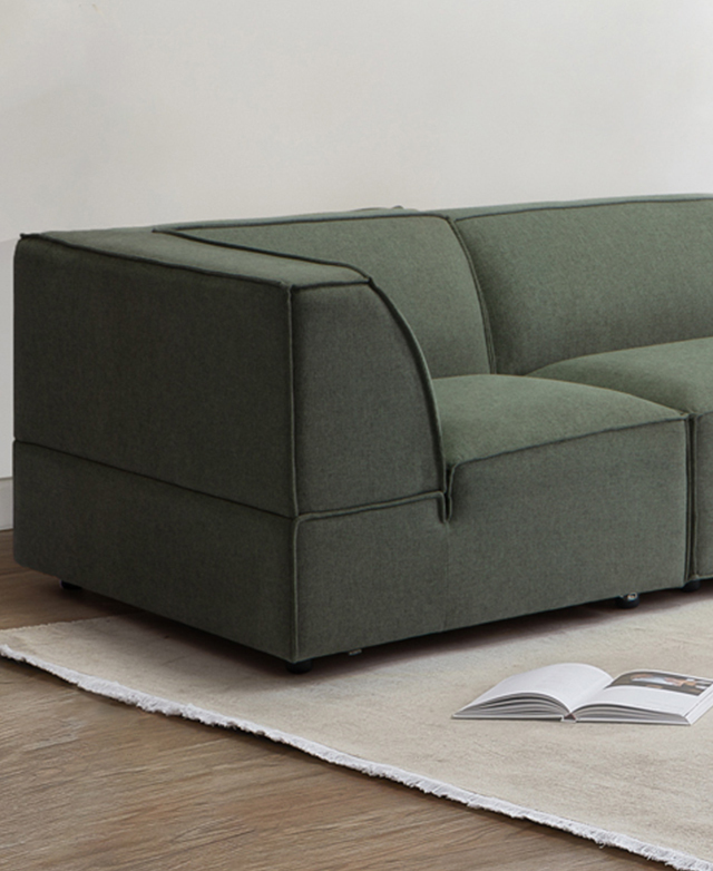 The corner end of the chunky green sofa is positioned on top of a flatweave cream rug, which has an open book on top. The corner end of the chunky green sofa is positioned on top of a flatweave cream rug, which has an open book on top.