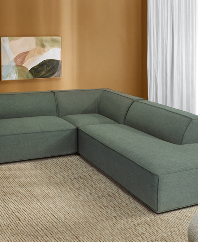 Rich yellow walls are the backdrop to a large, green L-shaped sofa on top of a taupe rug. Rich yellow walls are the backdrop to a large, green L-shaped sofa on top of a taupe rug.