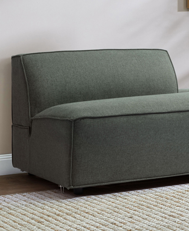 A close view of a modular section of a green sofa shows the thick seat, chunky backrest, and piping trims.