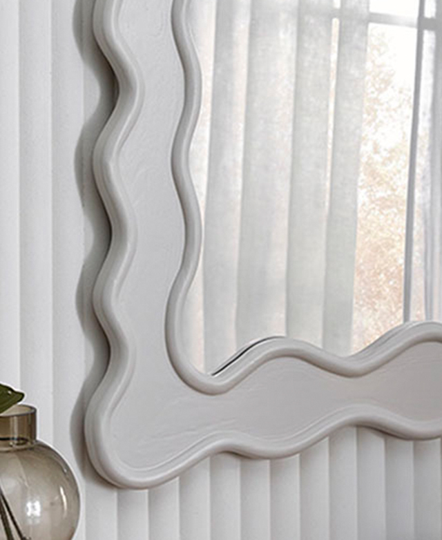 The mirror is shown against a white panelled wall; a corner of the smooth wavy frame  is shown.