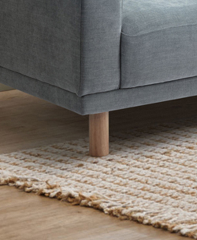Cropped view of the sofa shows a front leg on top of a cream and taupe rug.