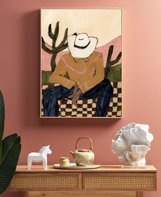 The desert-inspired wall art hangs over a small rattan and timber console table, which is topped with decorative items.