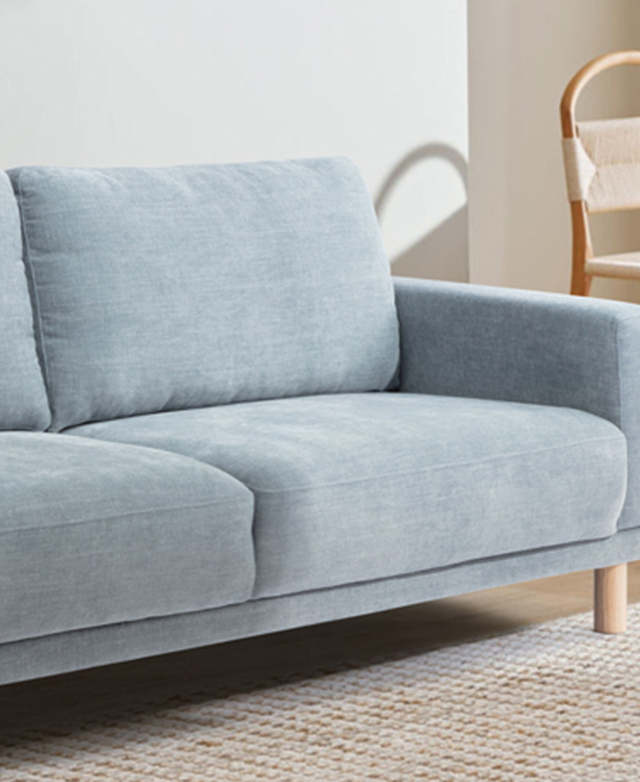 Three-quarter angle of one end of the blue commercial-grade sofa in a bright room on a jute rug.