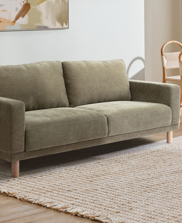 Three-quarter angle of the green commercial-grade sofa in a bright room on a jute rug.