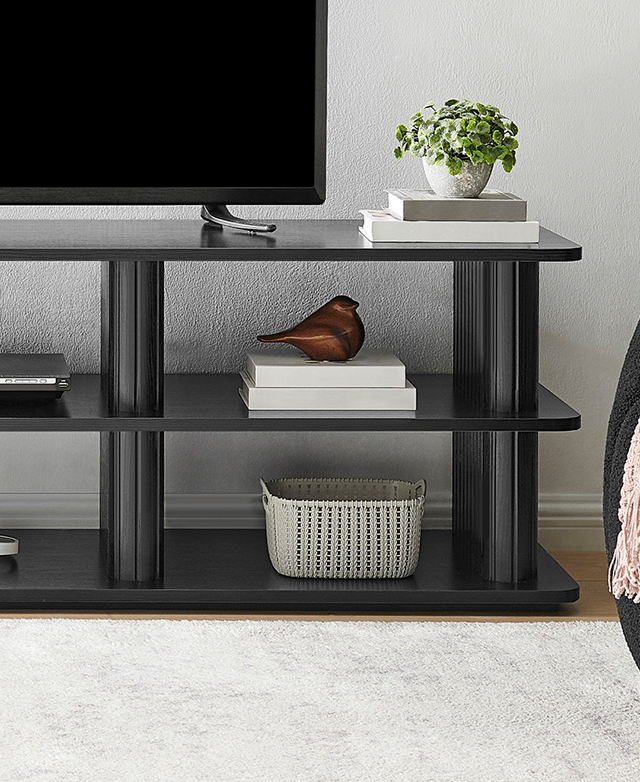 Shown in a white living room, the black TV unit is styled with decorative items, books, and topped with a TV.