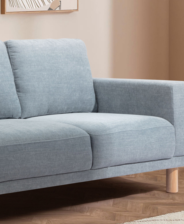 Three-quarter angle of one end of the blue commercial-grade sofa in a warmly-lit room on parquet flooring.