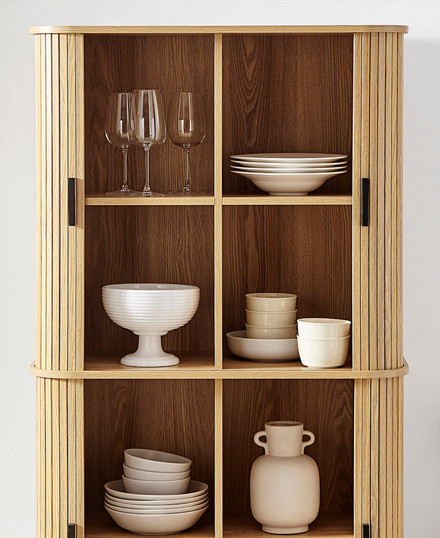 The flour sliding cupboard doors are open to showcase the shelves, which are filled with crockery and glassware. The flour sliding cupboard doors are open to showcase the shelves, which are filled with crockery and glassware.