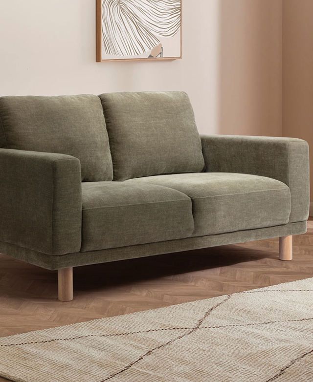 Three-quarter angle of the green commercial-grade sofa in a warmly-lit room next to a cream rug.
