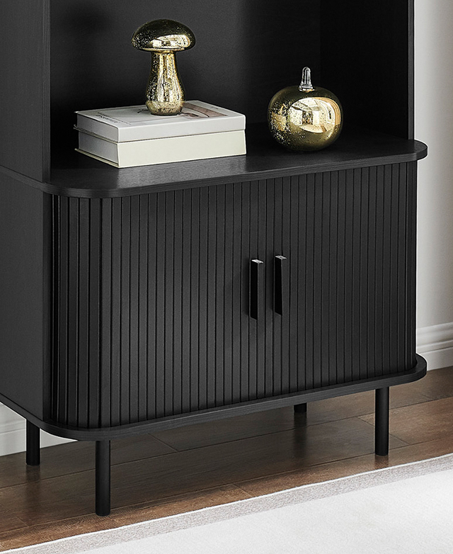 The bottom half of the bookcase has a rounded front with fluted detail, and books and decor are styled on the bottom shelf. The bottom half of the bookcase has a rounded front with fluted detail, and books and decor are styled on the bottom shelf.