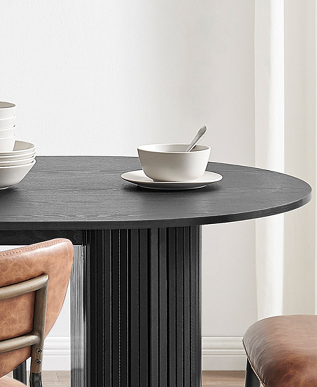 The black oval dining table is topped with white crockery in a bright room. The black oval dining table is topped with white crockery in a bright room.