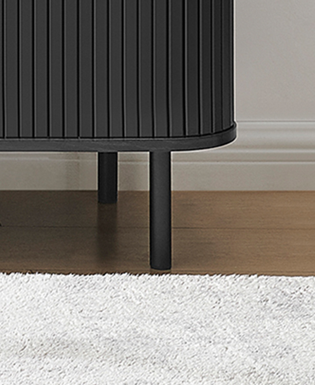Magnified view of one of the sleek black metal legs in front of a grey shag rug.