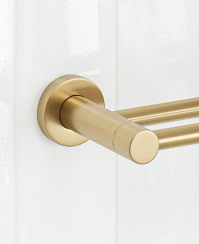 Gold double towel rail bracket on white tiles; round wall mount close-up.